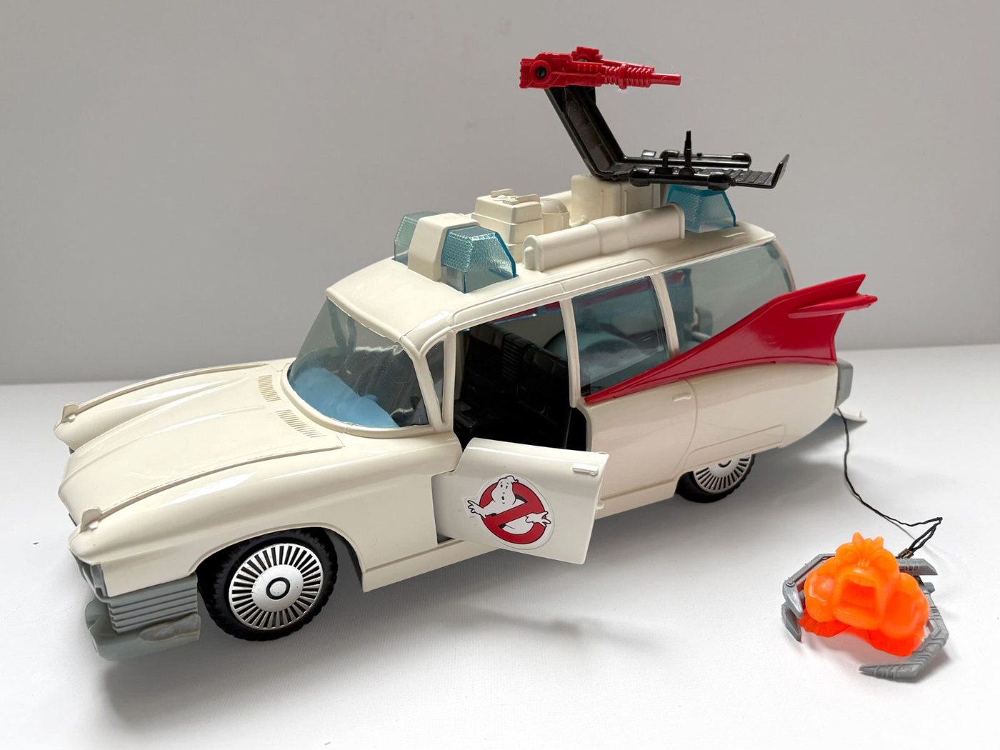 A Kenner Real Ghostbusters Ecto-1 photographed from the side with the driver's door open, the roof gun rack raised and the orange glow ghost beside it on its cable