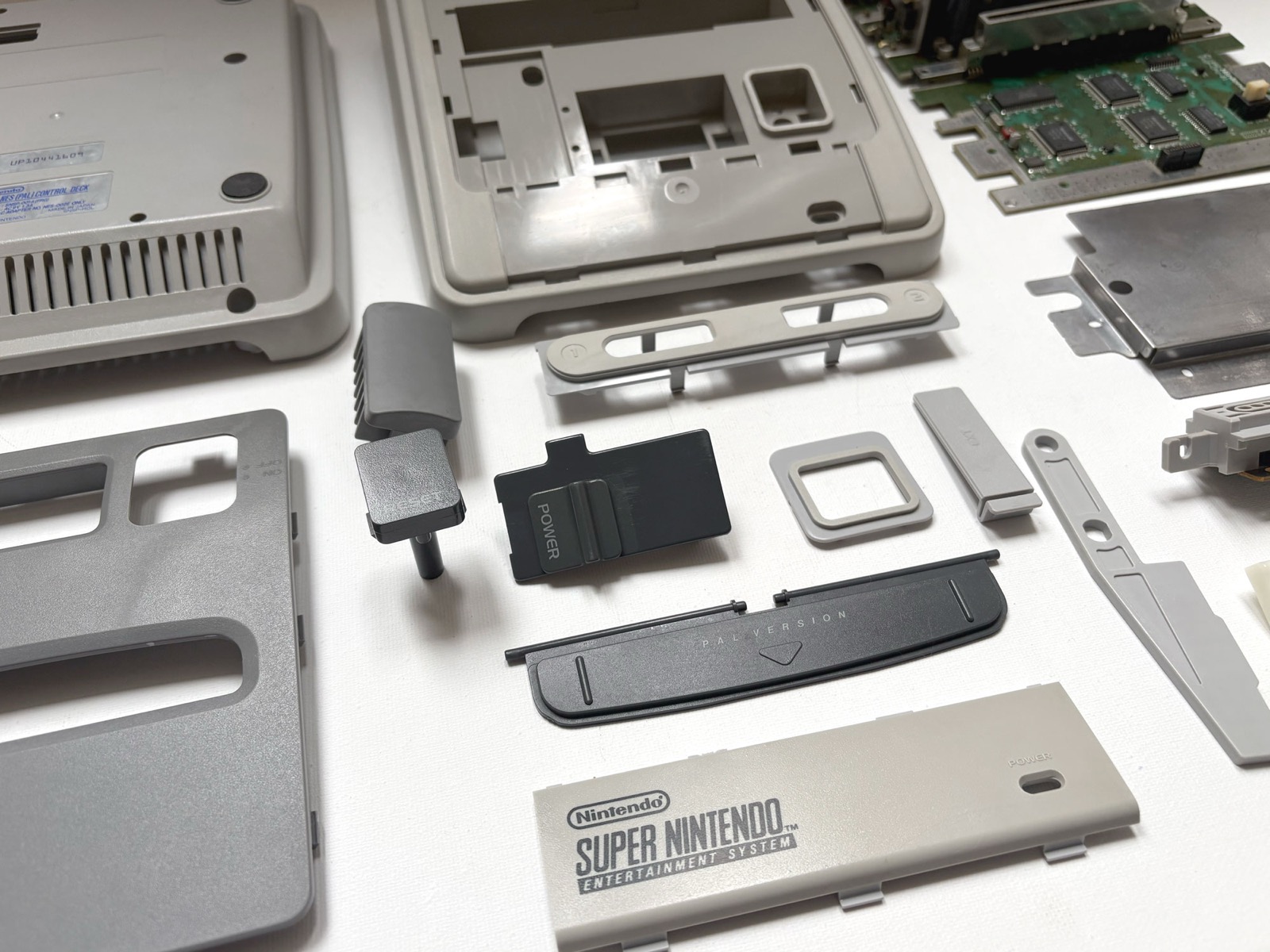 The treated mouldings at an angle: the power slide, the reset button, the EXT cover and the front badge plate, all back to grey, with the circuit board and the metal shield beside them.