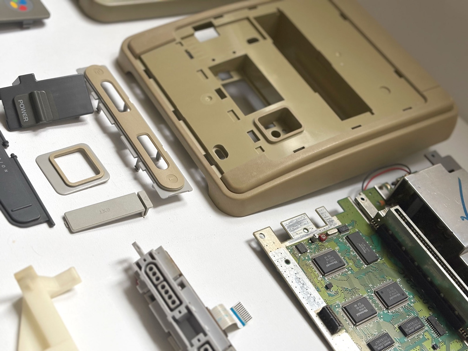 The yellowed upper shell seen at an angle with the smaller mouldings and the bare circuit board beside it. The shell is deep khaki while the controller port strips and the EXT cover next to it are noticeably paler.